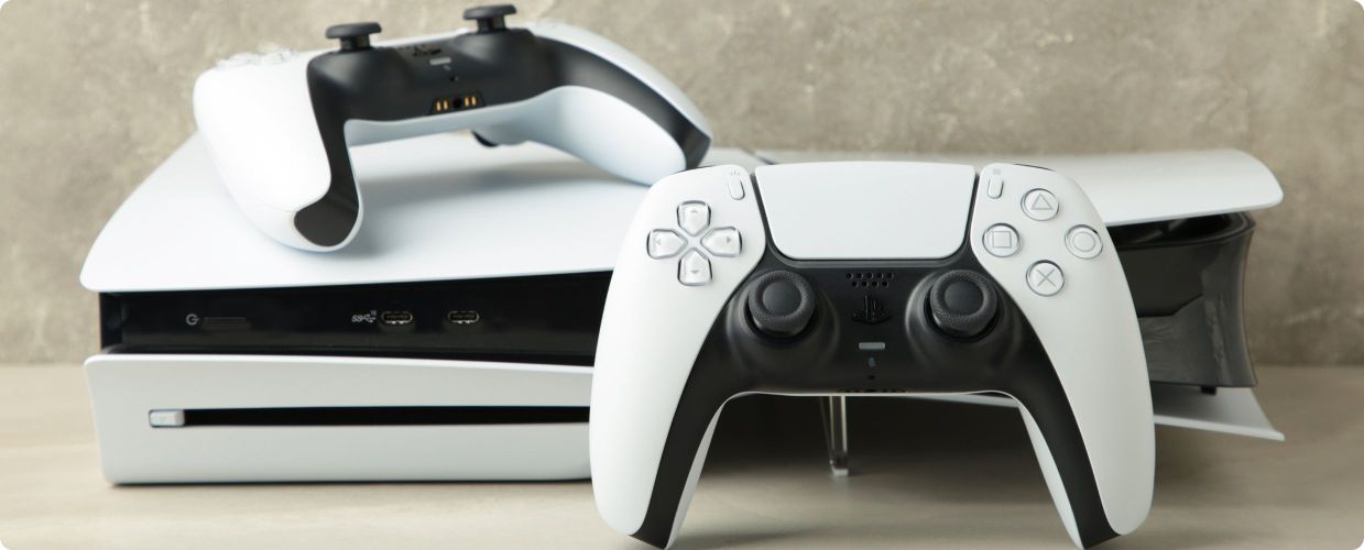 Biała konsola PlayStation 5 z napędem na płyty i dwa pady DualSense na jasnym blacie
