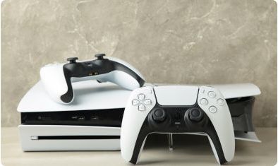 Biała konsola PlayStation 5 z napędem na płyty i dwa pady DualSense na jasnym blacie