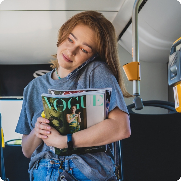 Kobieta w autobusie rozmawia przez telefon z ekranem chronionym szkłem prywatyzującym 3mk Privzone, trzymając magazyn Vogue